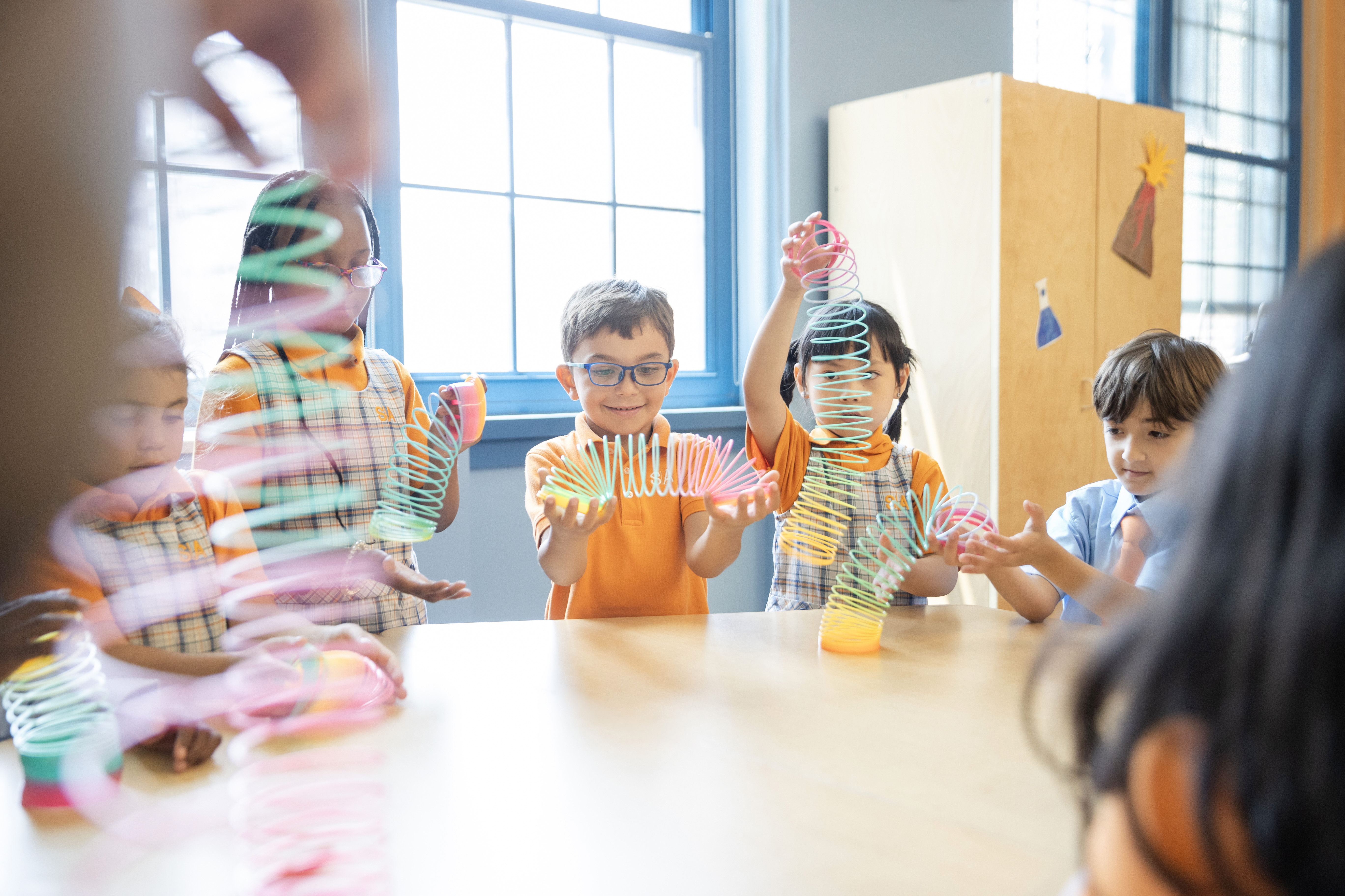 A group of students playing with colorful slinkys on a table.