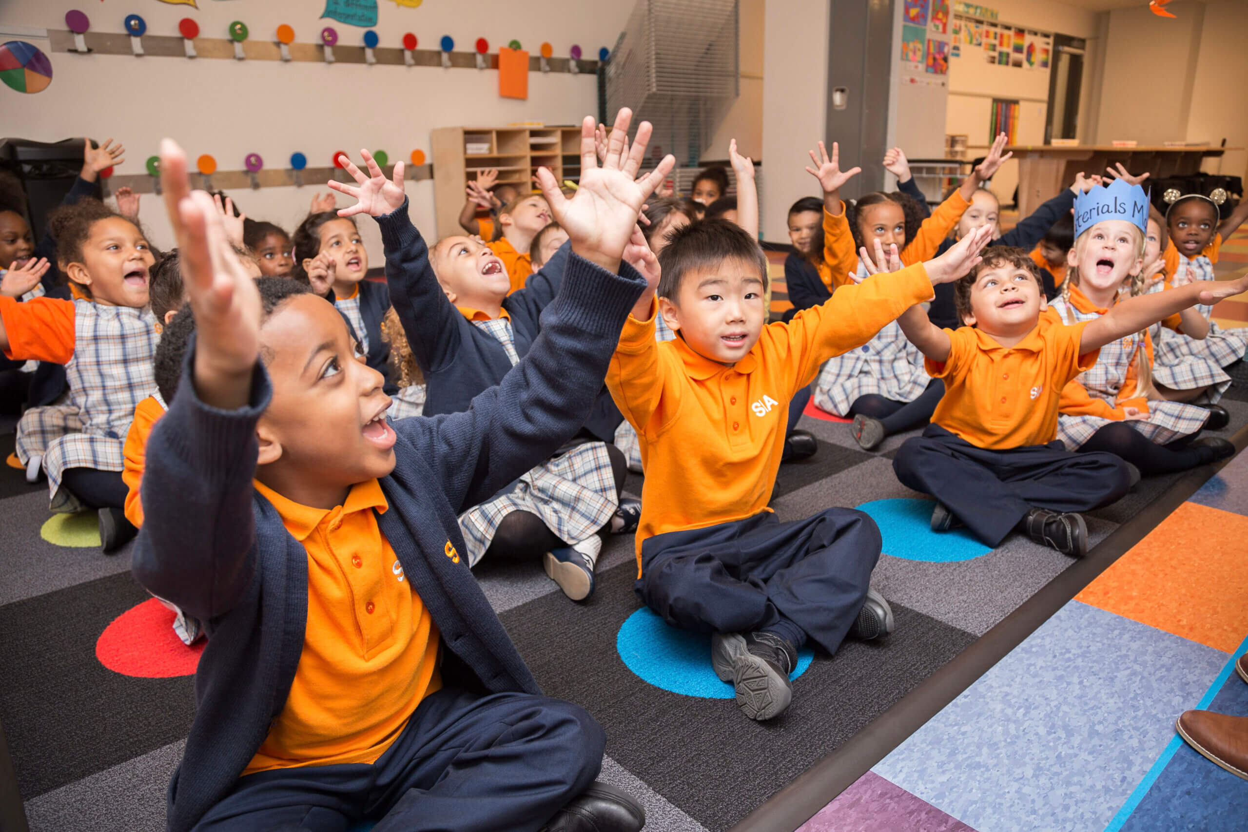 Group of kindergarten students sitting on a colorful rug and participating in a classroom activity.