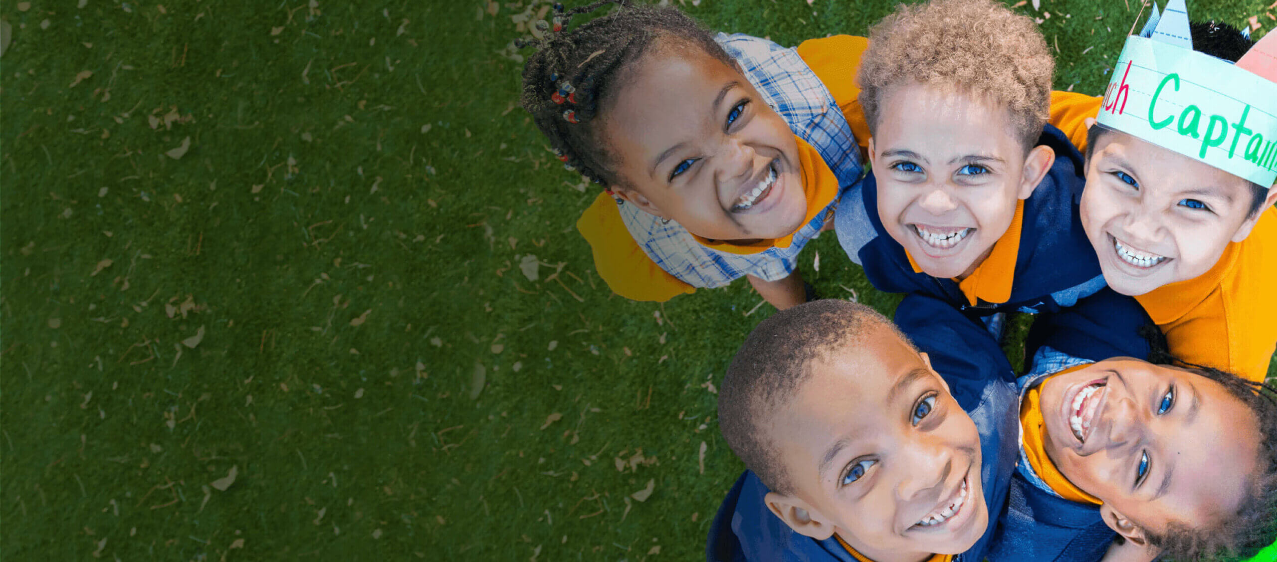 Children smiling in a circle on grass, wearing uniforms.