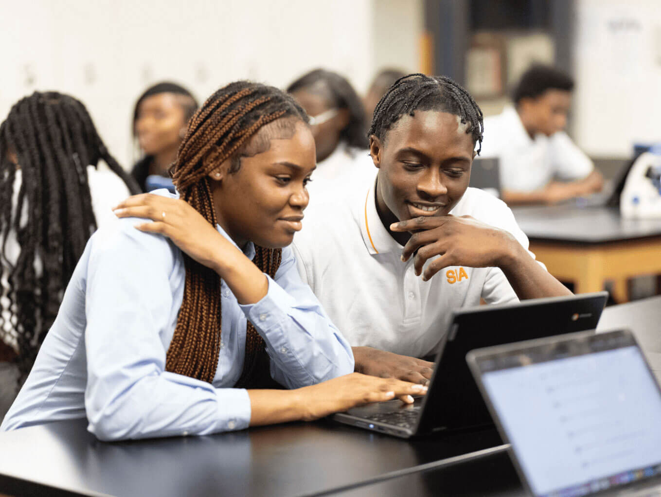 Two students collaborating at a laptop in a classroom.