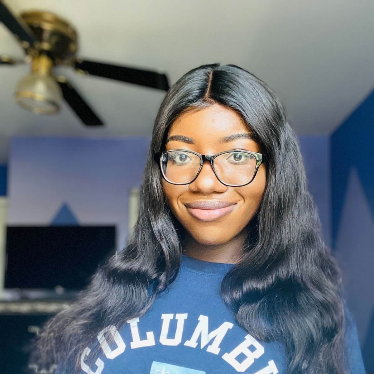 Person smiling, wearing glasses and "COLUMBIA" shirt, indoor room.