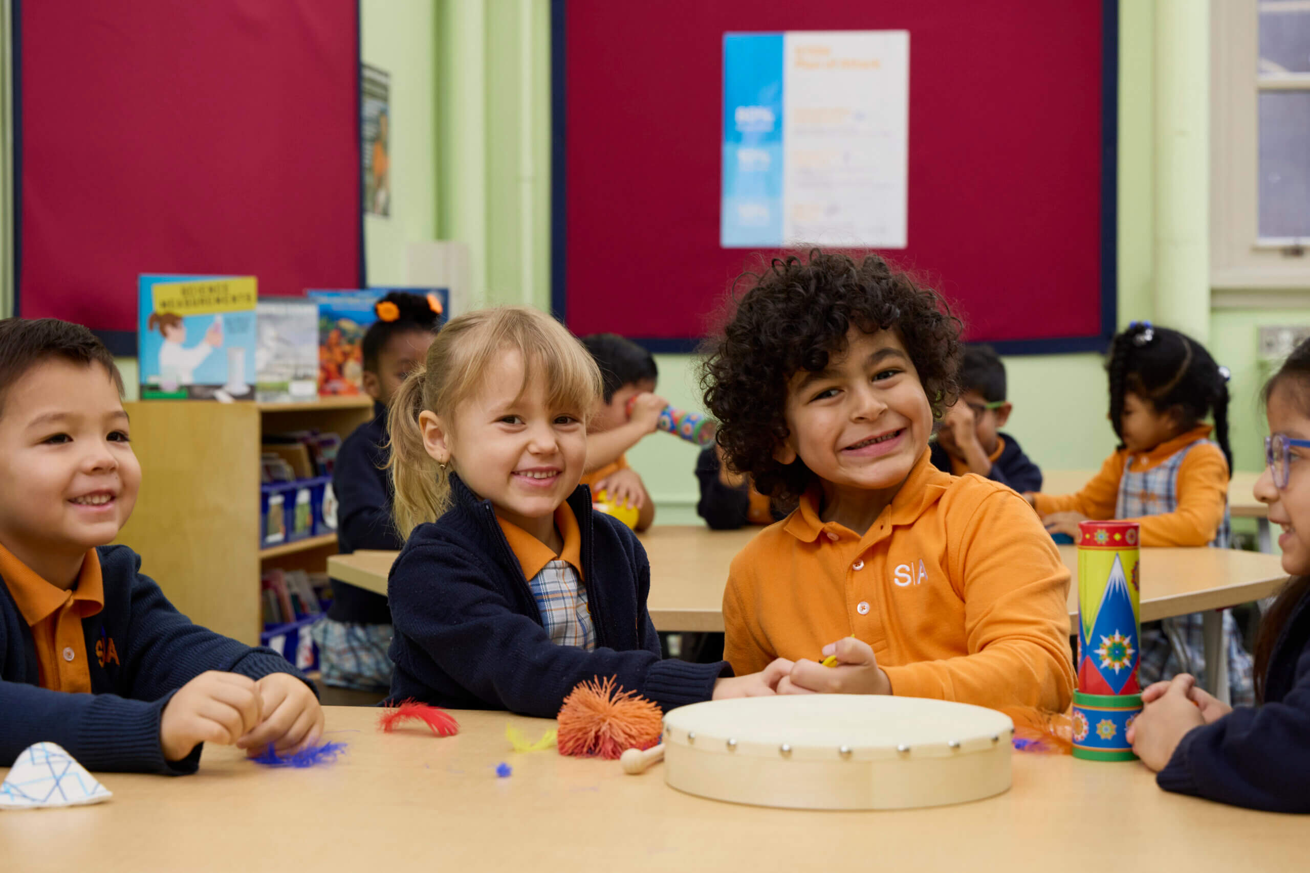 Young children sitting together at a classroom table, smiling and engaged in activities.