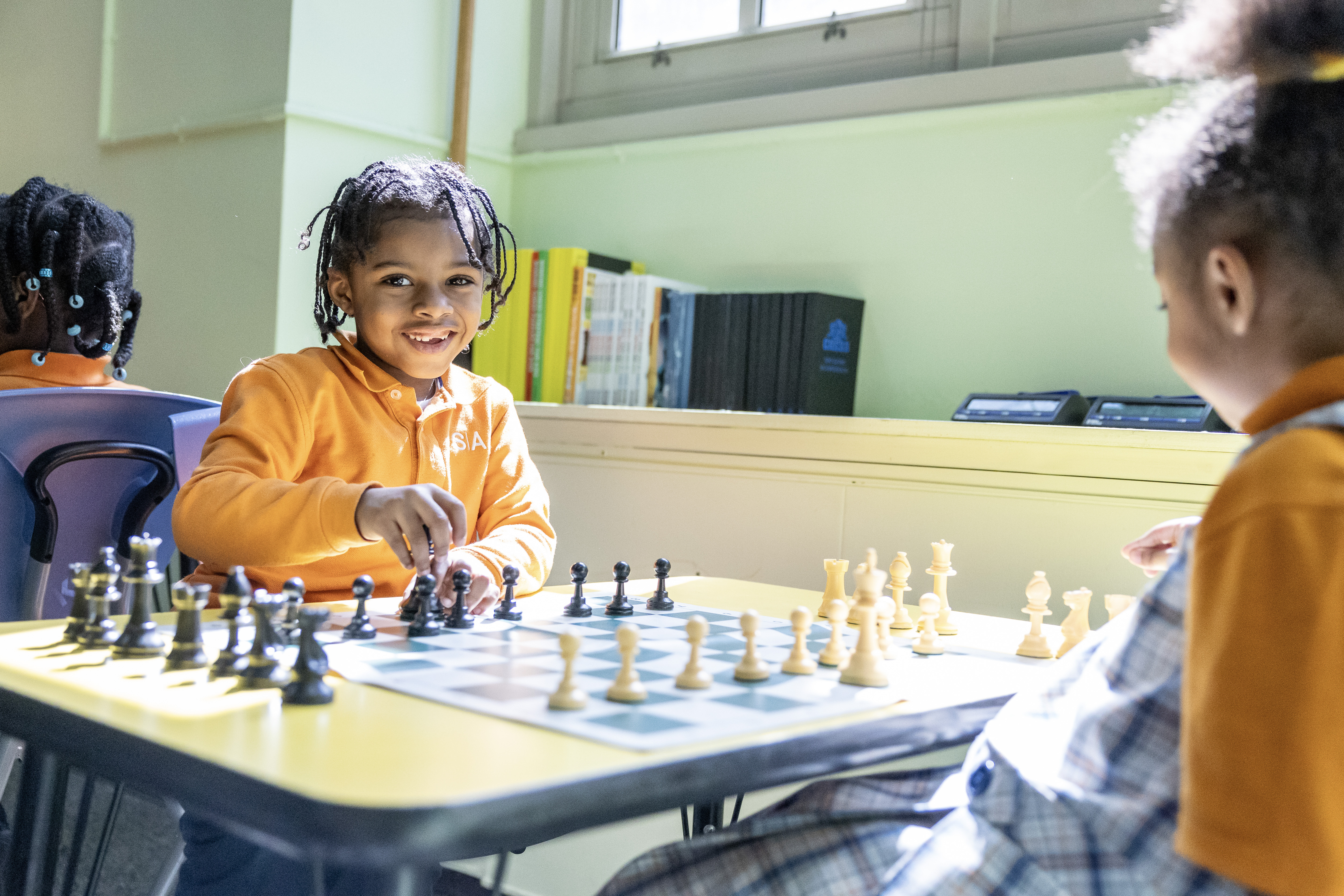 Children in a classroom smiling and playing chess together.