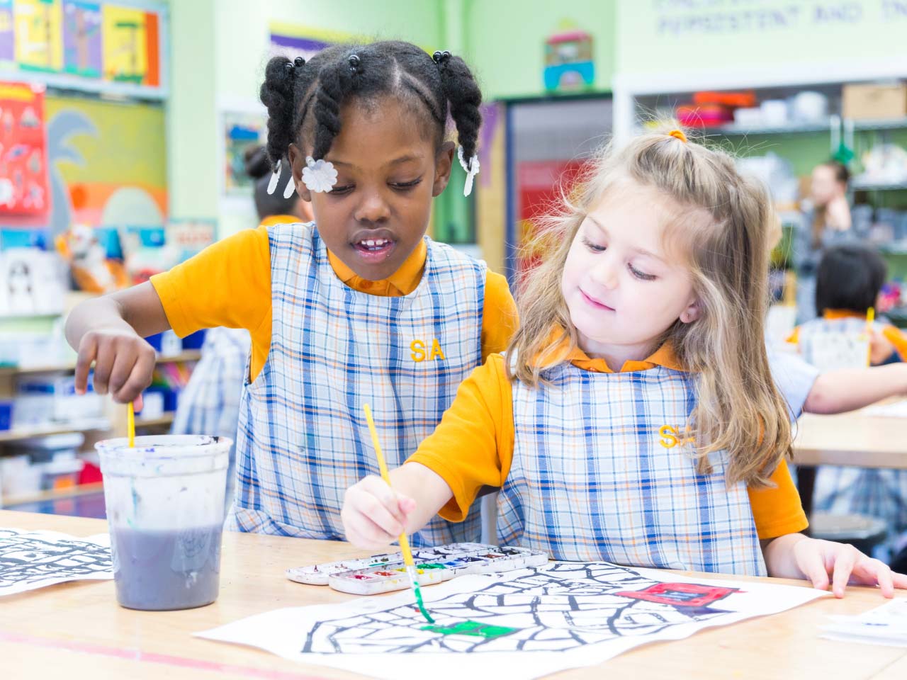 Children painting at a table in a colorful classroom.