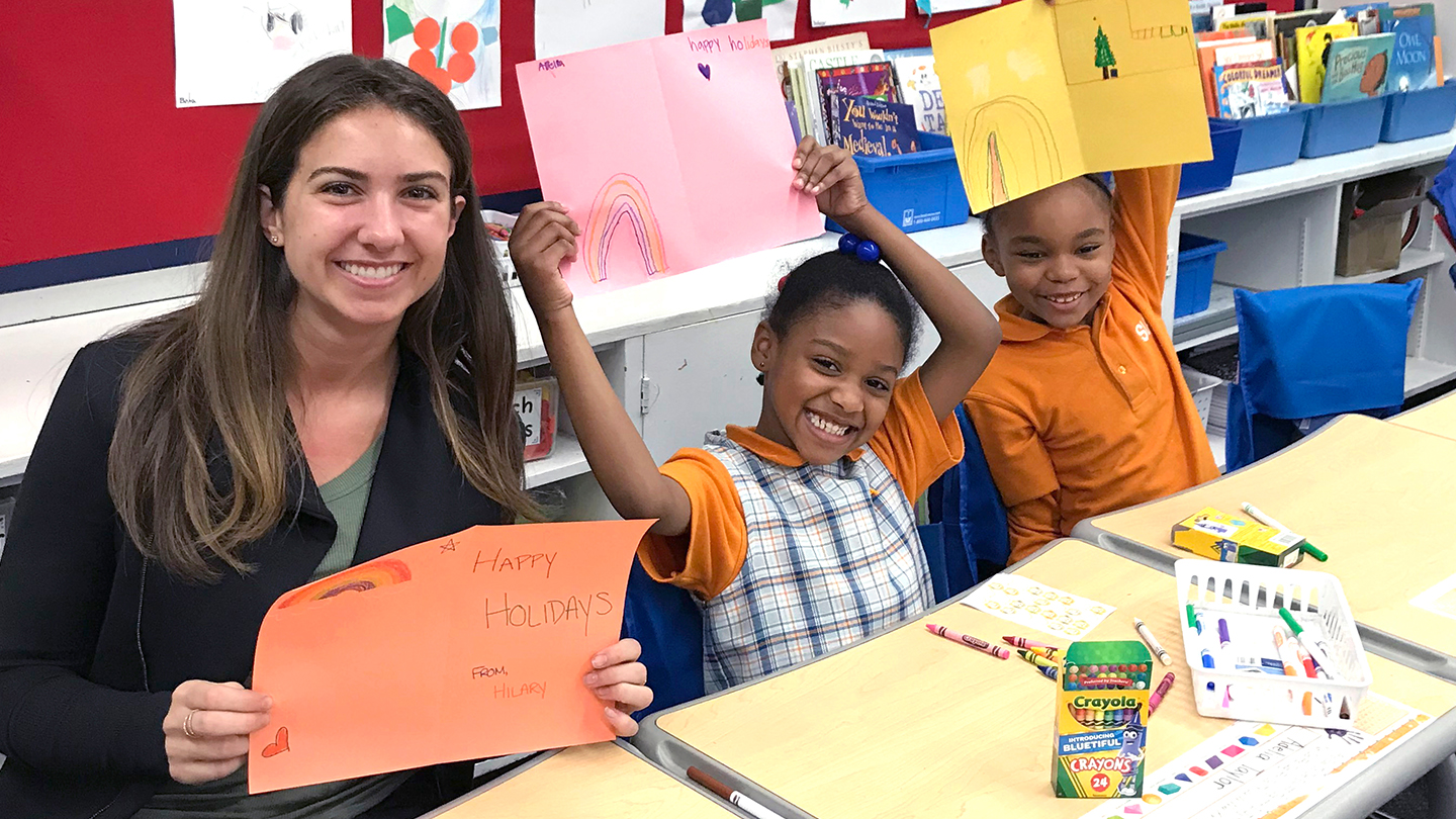 Teacher and two children holding holiday cards in classroom.